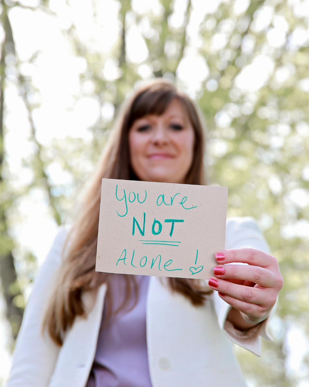 nurse practitioner holding a handwritten sign that says you are not alone. Healthcare provider who wants patients to know they are available and will listen when someone is in need.
